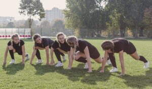 Cinco garotas se alongando em um campo aberto antes do treino de atletismo na Fredericton Christian Academy.