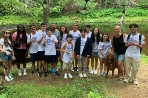 Grupo de estudantes com camisetas de acampamento escolar posando ao ar livre, representando cursos de verão.