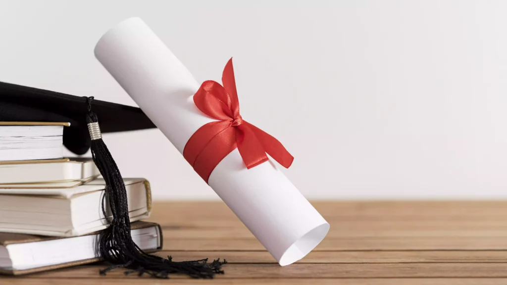 Diploma rolled up with red bow on pile of books and graduation cap, symbolizing the achievement of a Canadian Diploma.