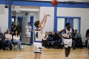 Estudantes da Fredericton Christian Academy jogando basquete com uniforme FCA Eagles em quadra interna, com público assistindo.