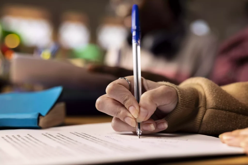 Student hand writing in proof with a blue pen, symbolizing the approval of studies in an academic environment.
