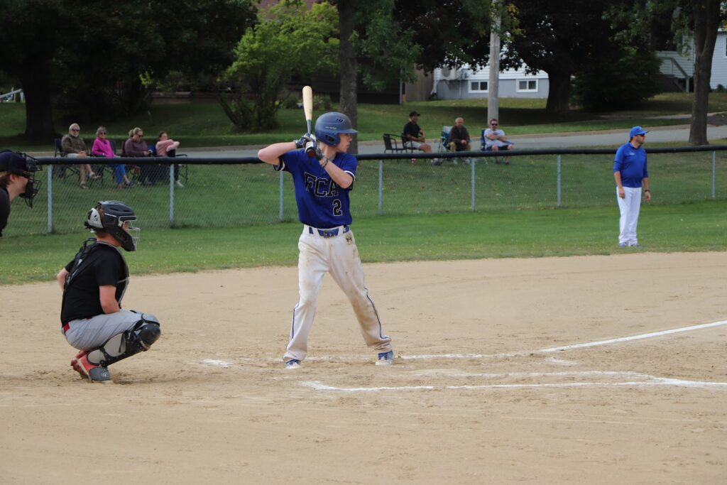 Student in blue uniform holding bat baseball player on the field, ready to bat, representing the practice of Optional Subjects.