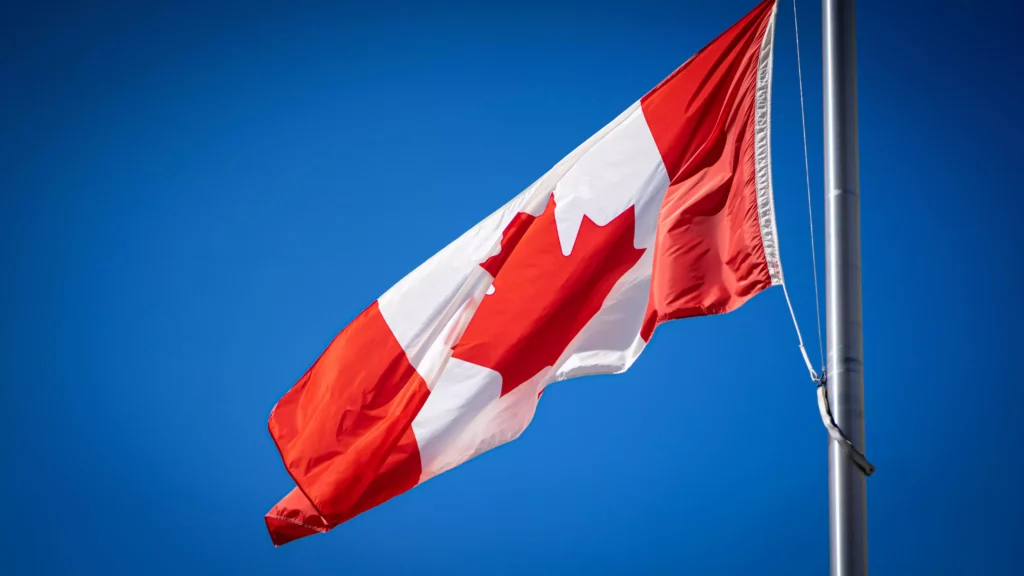 Bandeira do Canadá tremulando no mastro sob céu azul, representando o programa Mini High School da Fredericton Christian Academy.