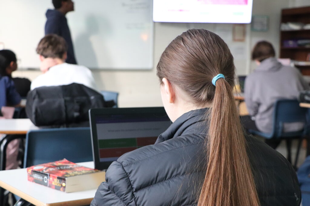 Student using notebook in classroom with books next to it, representing the focus on college preparation.