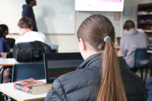 Estudante usando notebook em sala de aula com livros ao lado, representando o foco na preparação universitária.