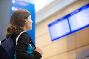 Jovem com mochila olhando painel de voos em aeroporto, representando o serviço de recepção no aeroporto para estudantes internacionais no Canadá.