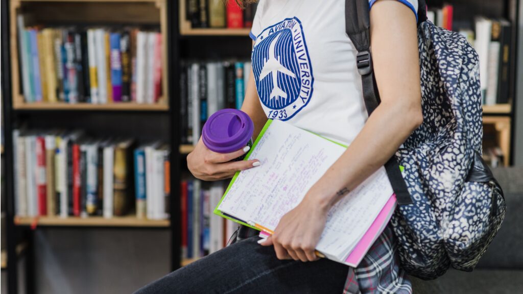 Jovem estudante com mochila nas costas segura caderno e copo reutilizável em ambiente acadêmico, representando atividades de registro acadêmico.