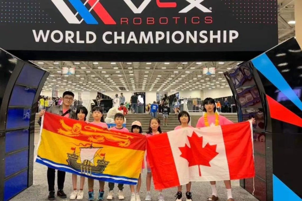 Grupo de estudantes com bandeiras do Canadá e New Brunswick participando do Campeonato Mundial de Robótica, representando as atividades extracurriculares da escola.
