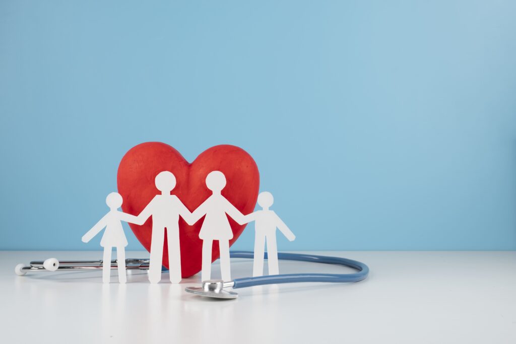 Representação simbólica de uma família com figuras de papel, coração vermelho e estetoscópio, destacando o cuidado com a saúde familiar no Canadá e o seguro saúde.