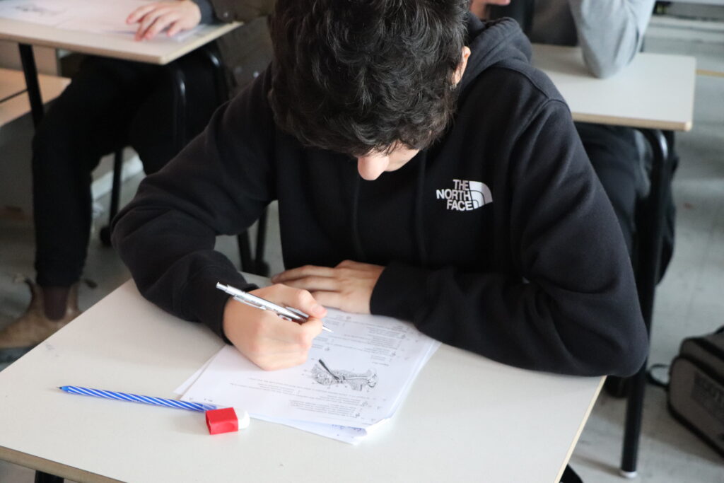Concentrated student writing on exam with pencil and eraser on the table, representing the Academic Validation process.