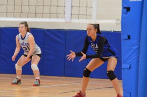 Estudantes da Fredericton Christian Academy em quadra de vôlei, prontas para receber o saque adversário.
