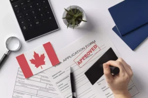 Formulário de solicitação de visto canadense aprovado com carimbo, ao lado de passaportes, bandeira do Canadá e calculadora.