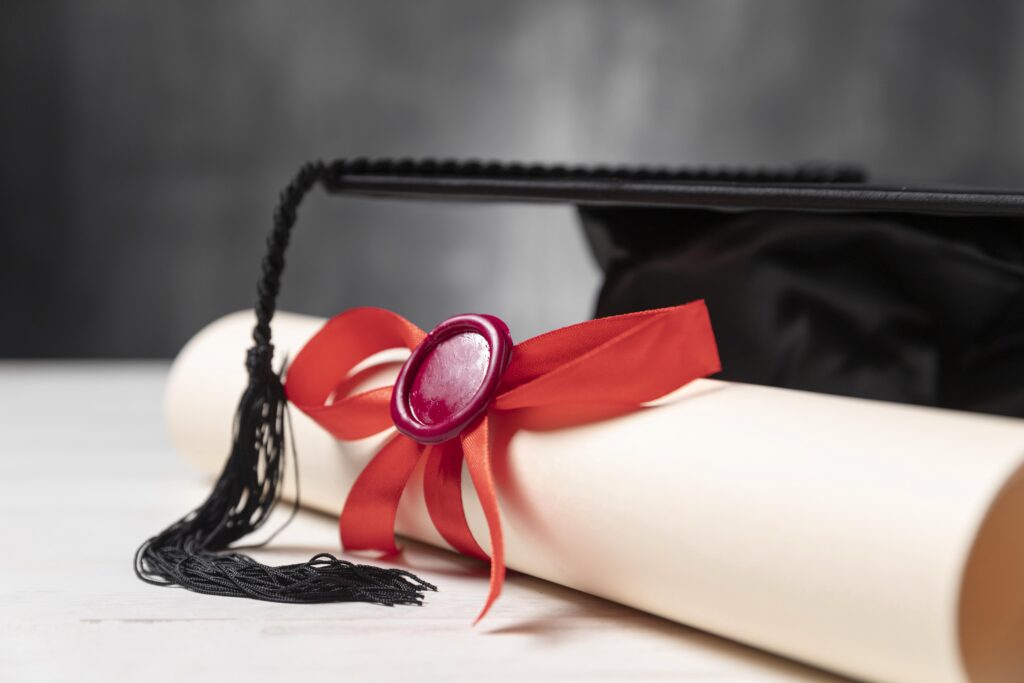 Bachelor's diploma with red wax seal and black graduation cap on a light table.