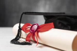Diploma de bacharelado com selo de cera vermelha e chapéu de formatura preto sobre uma mesa clara.