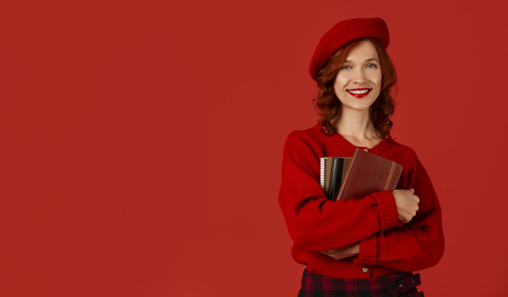 Estudiante sonriente de habla francesa con cuadernos sobre fondo rojo
