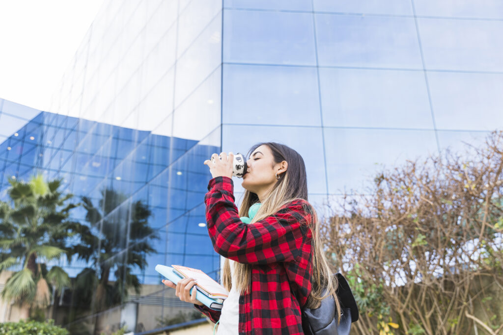 UCC (Upper Campus on Canada Street) student having coffee in front of modern building with glass facade