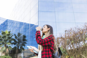 Estudante UCC (Upper Campus on Canada Street) tomando café em frente a prédio moderno com fachada de vidro