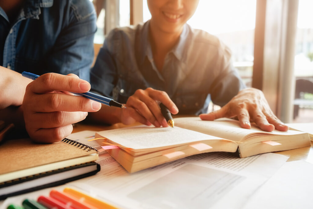 Two university students studying together with books and notes on the table in a bright environment.