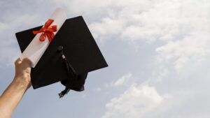 Mão segurando capelo e diploma de graduação com céu ao fundo